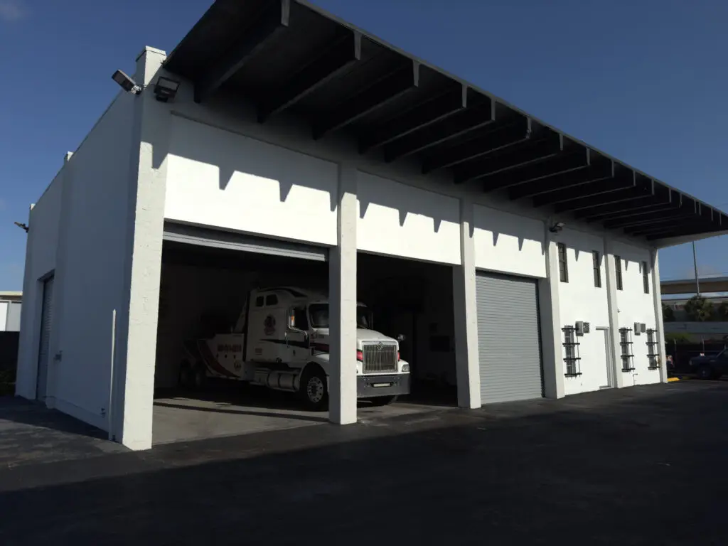 A white tow truck is parked in a truck repair shop, illustrating the establishment's role in servicing and maintaining vehicles.